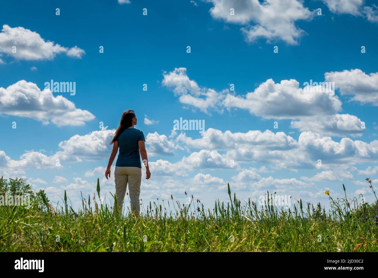Frau auf der Spitze des Hügels mit Blick auf den blauen Himmel mit Wolken. Symbol für Träumen, Erfolg und Selbstverbesserung Stockfoto