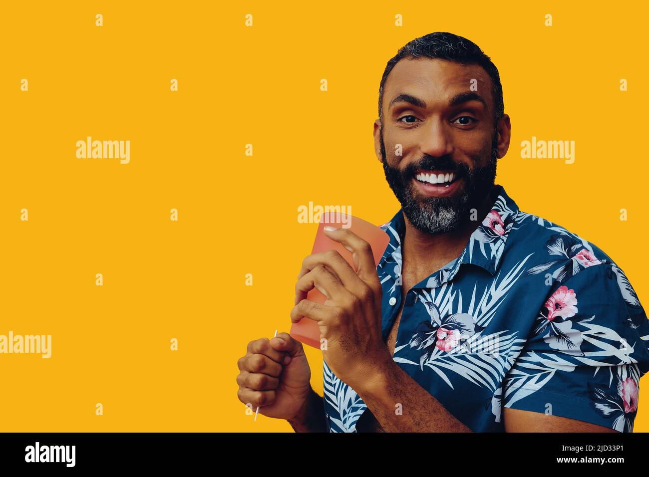 Glücklich lächelnder afroamerikanischer Mann, der ein hawaiianisches Hemd mit einem Cocktail-Glas-Studiofoto trägt Stockfoto