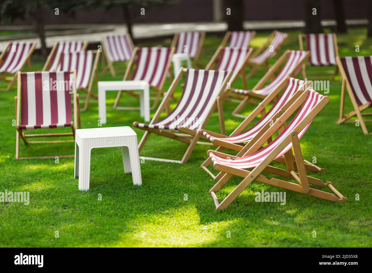 Gestreifte Sonnenliegen und ein Tisch im Park auf dem Rasen. Das Konzept der Erholung und Outdoor-Aktivitäten. Stockfoto