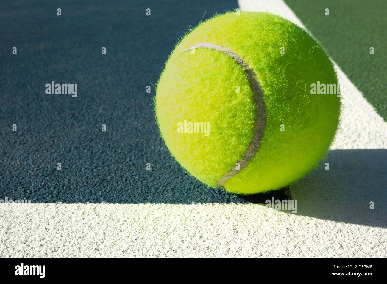 Nahaufnahme eines Tennisballs, der an einem sonnigen Tag in einer gemalten Linie auf einem Hartplatz sitzt Stockfoto