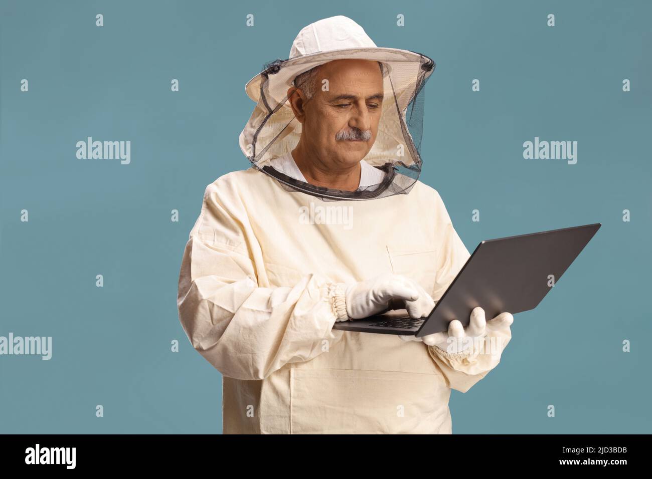 Reifer Bienenhalter in Uniform mit einem Laptop-Computer auf blauem Hintergrund isoliert Stockfoto