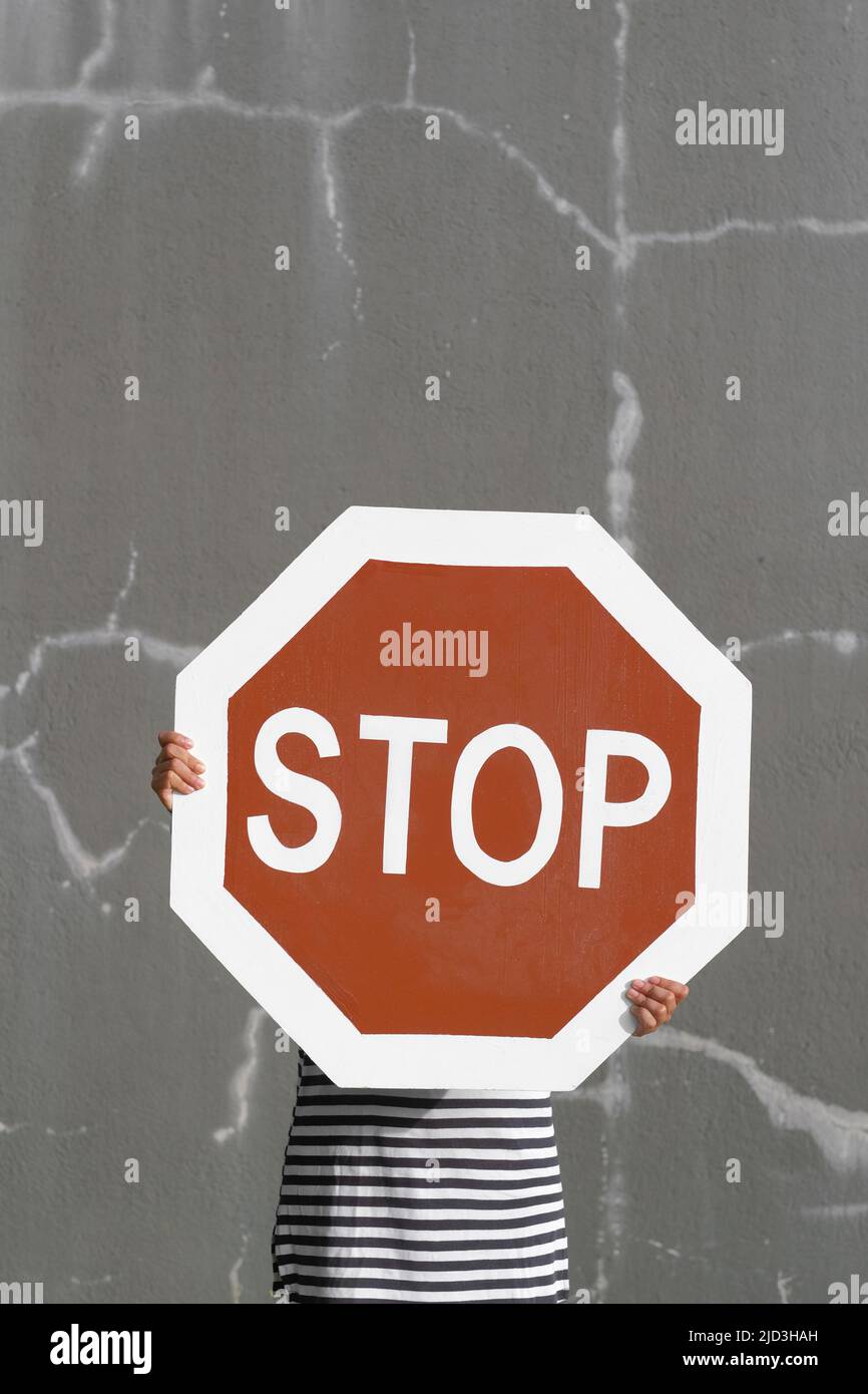 Person hält großes Stoppschild. Kräftiges Rot gegen die rissige graue Wand. Auffälliges Symbol für abstrakte Konzepte: Toxisches Verhalten und Negativität. Stockfoto