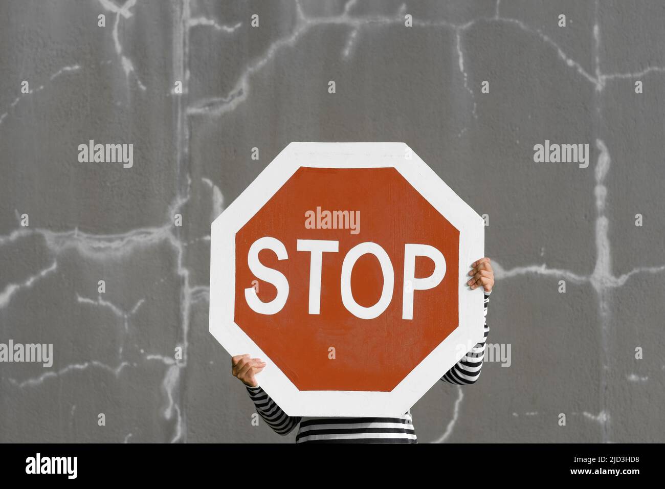 Person hält großes Stoppschild. Kräftiges Rot gegen die rissige graue Wand. Auffälliges Symbol für abstrakte Konzepte: Toxisches Verhalten und Negativität. Stockfoto