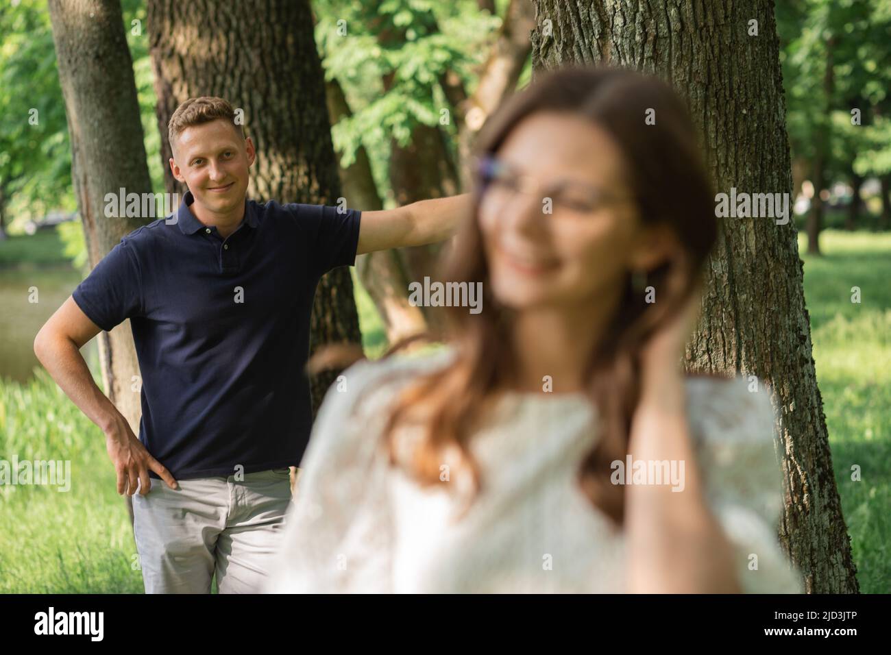 Defokussieren Frau auf Mann im Park zwischen Bäumen, glückliche Menschen Spaß am Sommertag, Paar verliebt Stockfoto