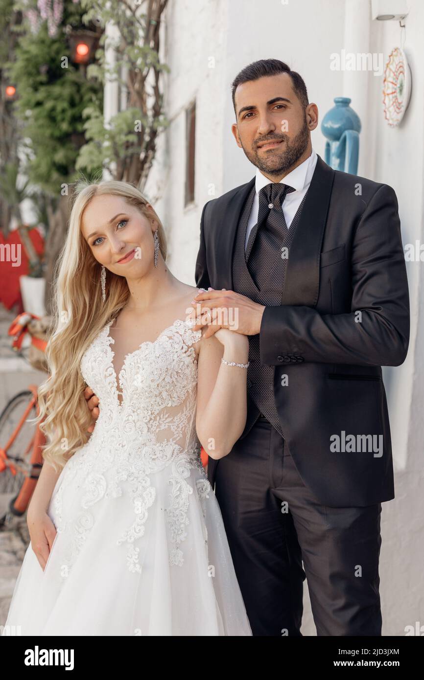 Vertikales Porträt Fröhliches und romantisches Ehepaar, blonde Frau, schwarzhaariger Mann bei der Hochzeitszeremonie. Feiertagsfeier Stockfoto