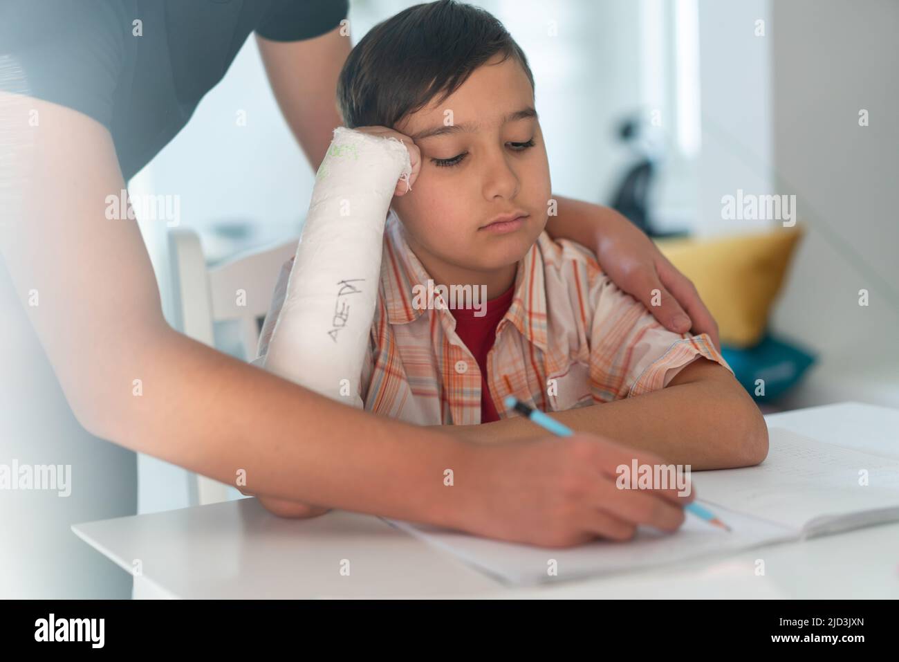 Junge mit gebrochenem Arm in Gips, der Hilfe von einem älteren Bruder für die Hausaufgaben hat. Hochwertige Fotos Stockfoto