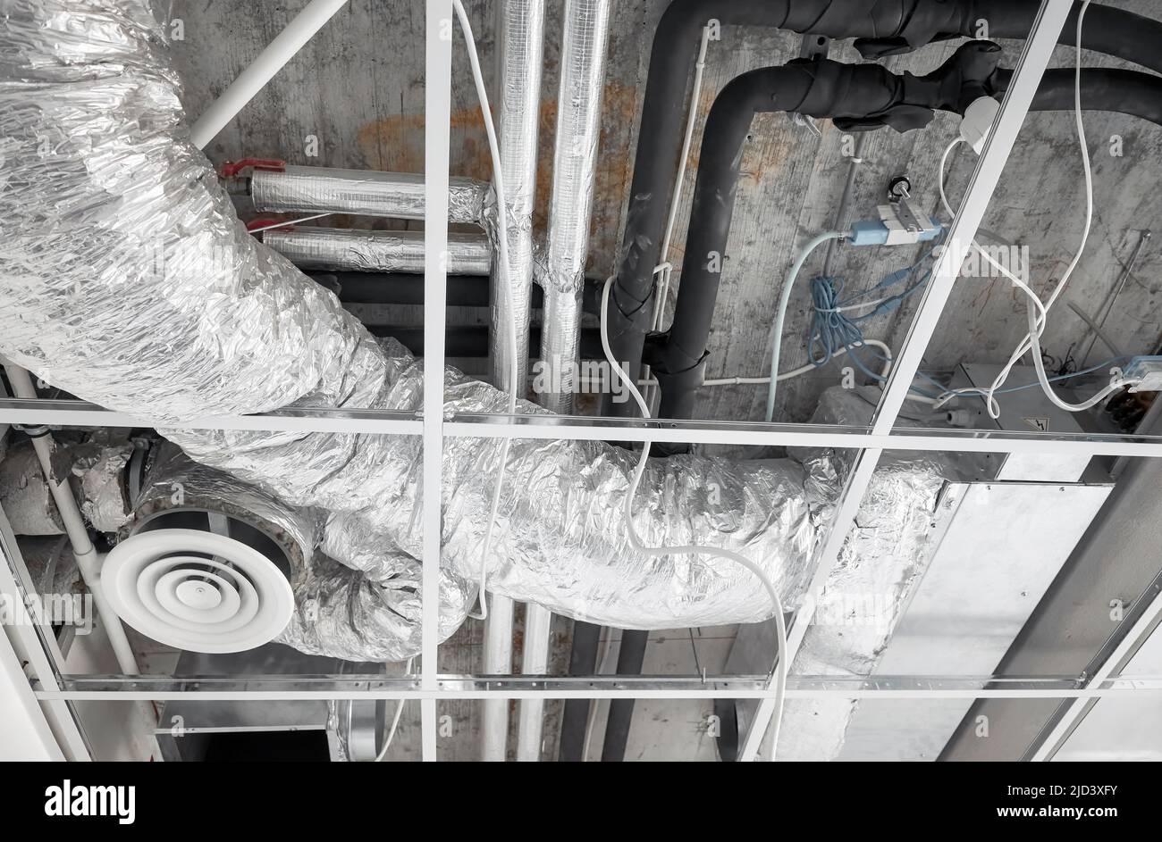 Belüftungssystem mit Rohren aus silbernem Dämmmaterial in abgehängter Decke während der Renovierung. Stockfoto