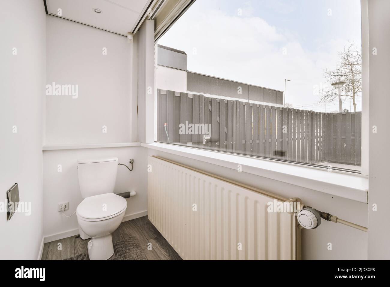 Schmale weiße Toilette mit Heizkörper unter dem großen Fenster Stockfoto