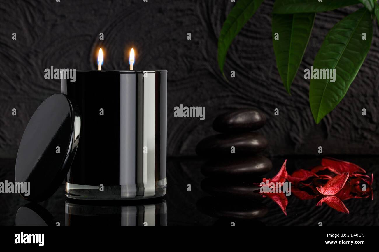 Brennende schwarze Kerzen und Spa-Steine auf schwarzem Hintergrund, Nahaufnahme. Spa-Komposition. MODELL Stockfoto