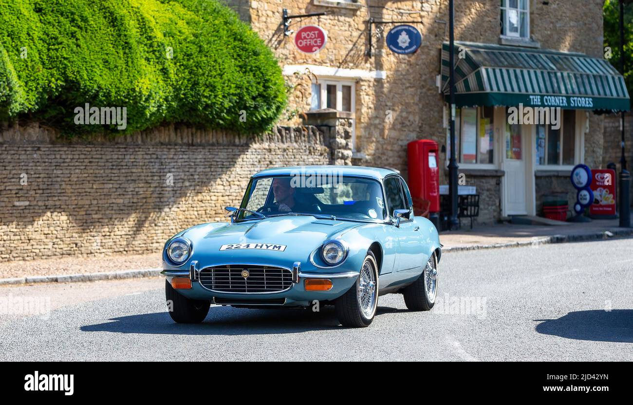 1972 blauer Jaguar vom Typ E, der durch ein englisches Dorf fährt Stockfoto