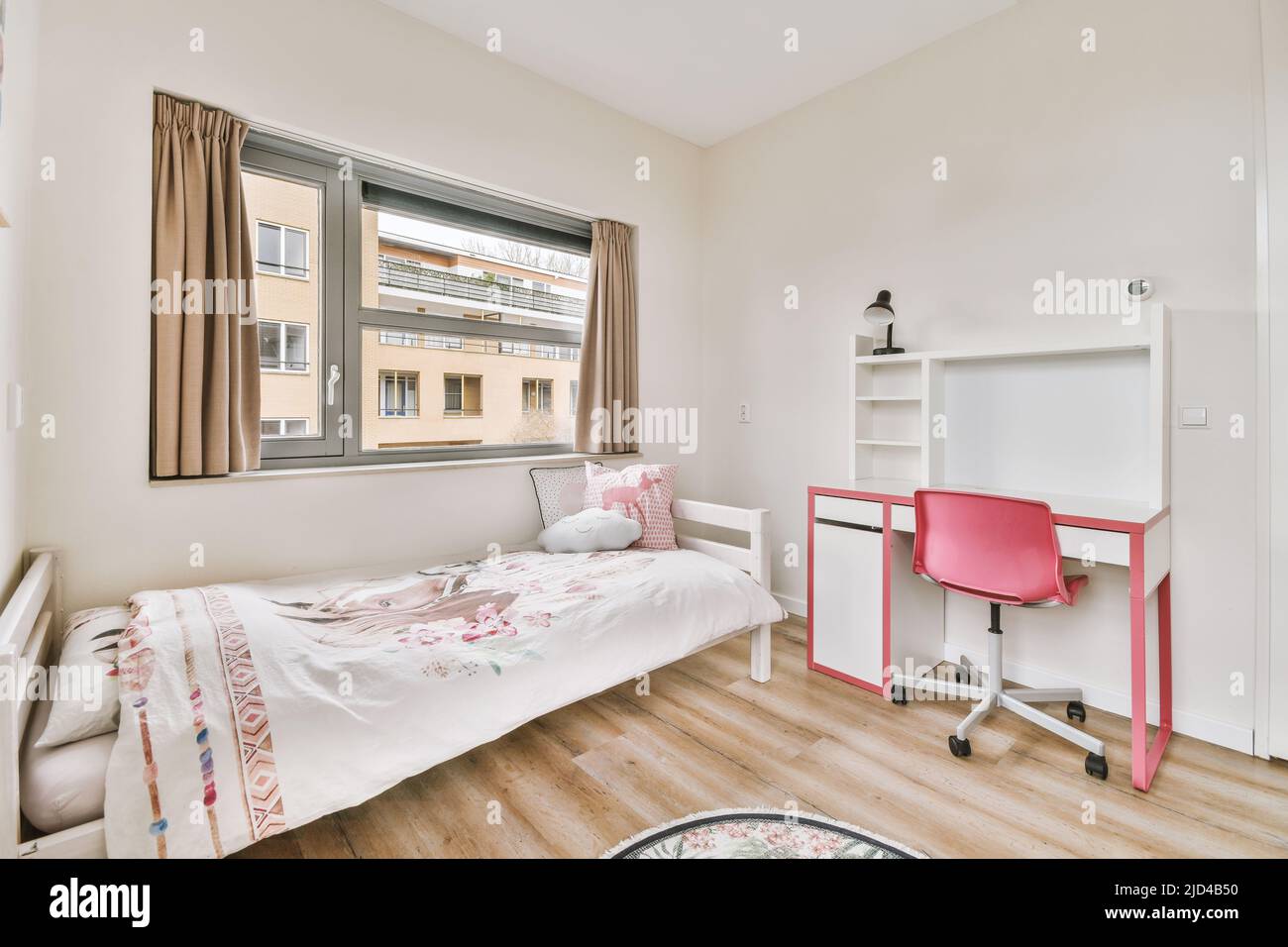 Das Innere eines modernen Kinderzimmers mit großen Fenstern, mit einem Bett und einem Tisch mit einem leuchtend rosa Sessel Stockfoto