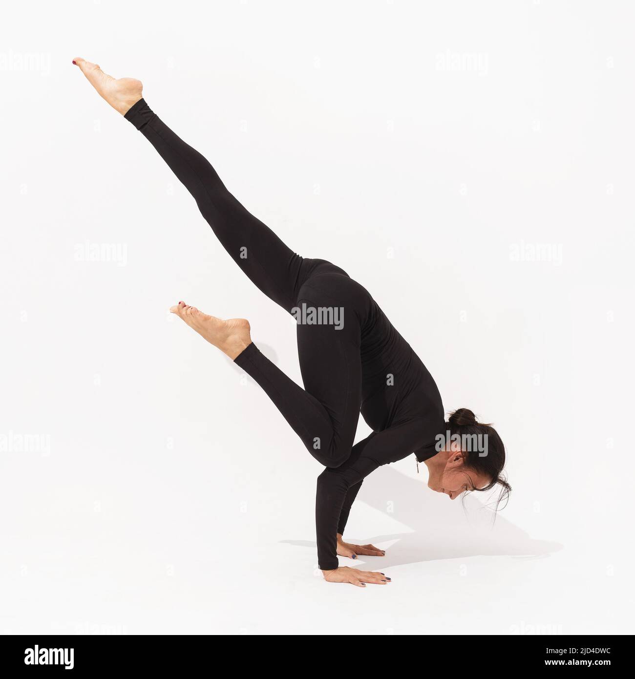 Frau, die Yoga praktiziert, führt die Übung Eka Pada Bakasana durch, Kranstellung mit ausgestrecktem Bein, Training in schwarzer Sportkleidung auf weißem Hintergrund Stockfoto