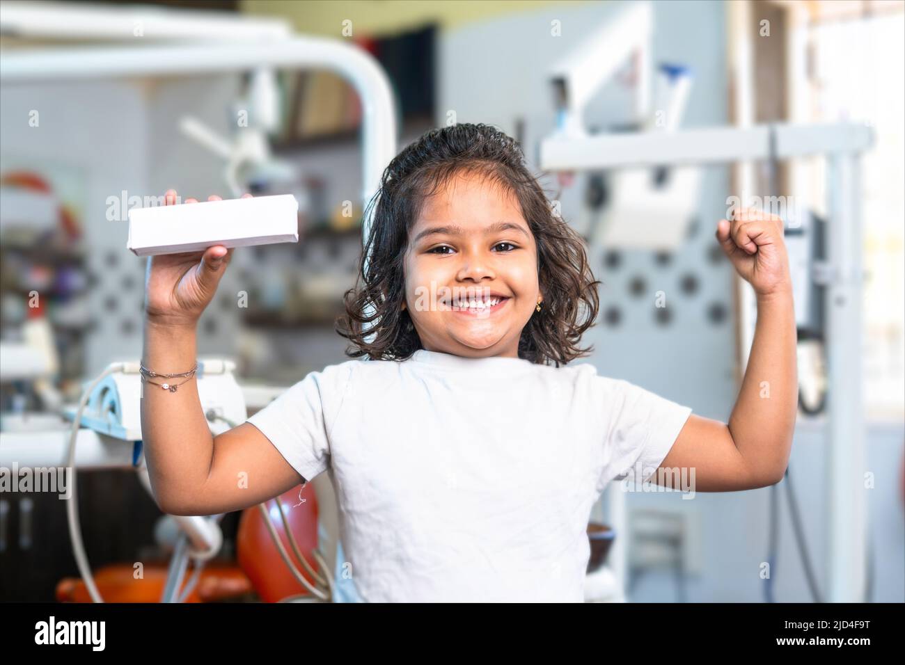 Glückliches lächelndes Mädchen zeigt Muskelkraft, indem sie Zahnpasta beim Blick auf die Kamera hält - Konzept von Wellness, pudrvolle Zähne und Medicare Stockfoto