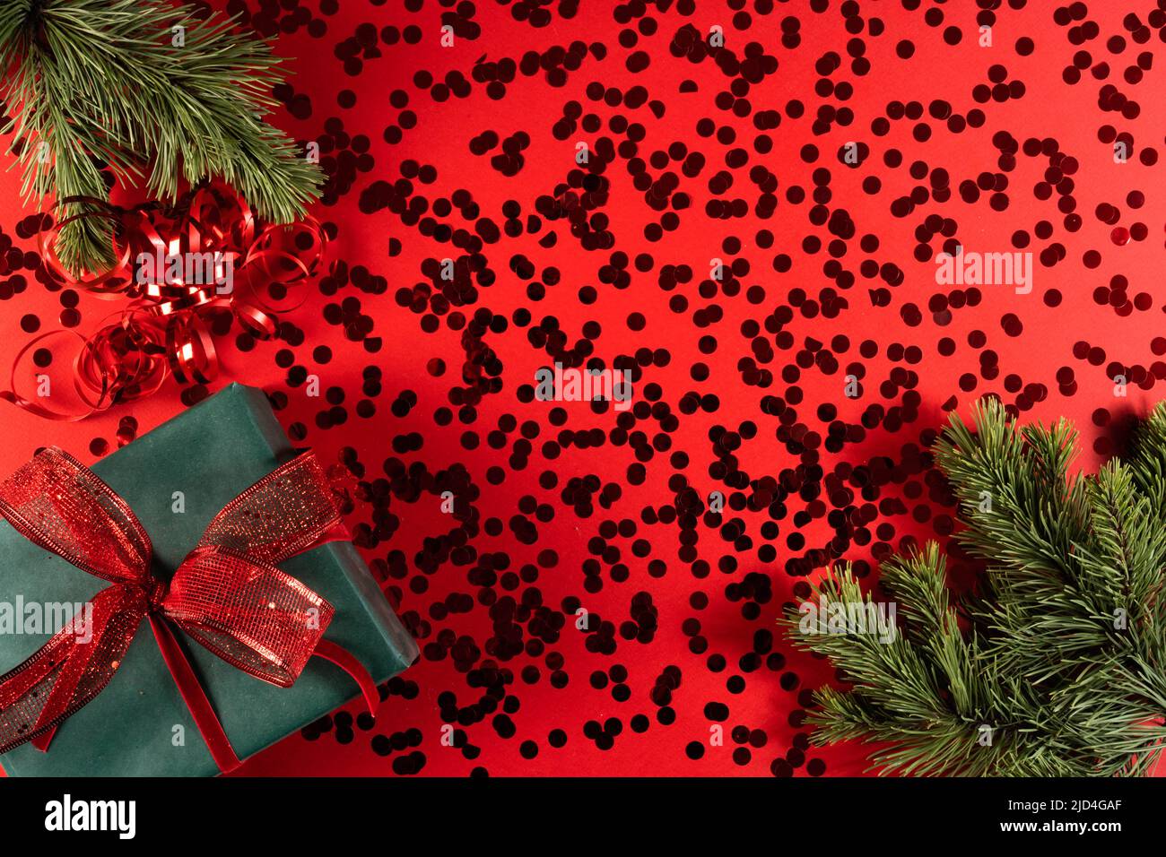 Eine grüne Geschenkbox mit einer roten Schleife auf einer roten mit Konfetti und einem Tannenzweig. Das Konzept von Weihnachten und Neujahr, Familienurlaub. Stockfoto