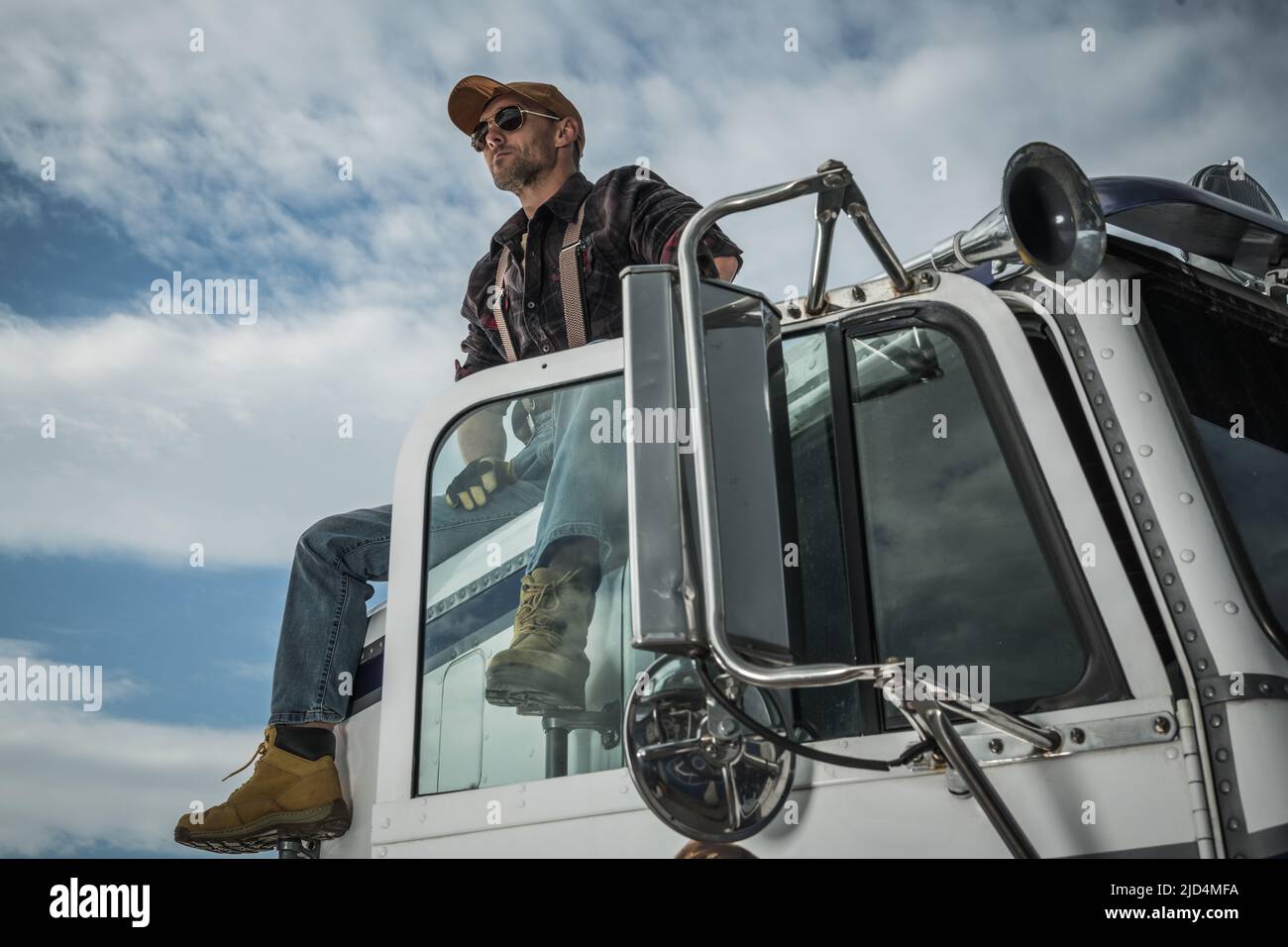 Stolzer kaukasischer Lkw-Fahrer bei seinem 40s auf dem Dach der Kabine seines alten Semi-Truck-Fahrzeugs sitzend, genießt den Moment der Ruhe während der Route. Stockfoto