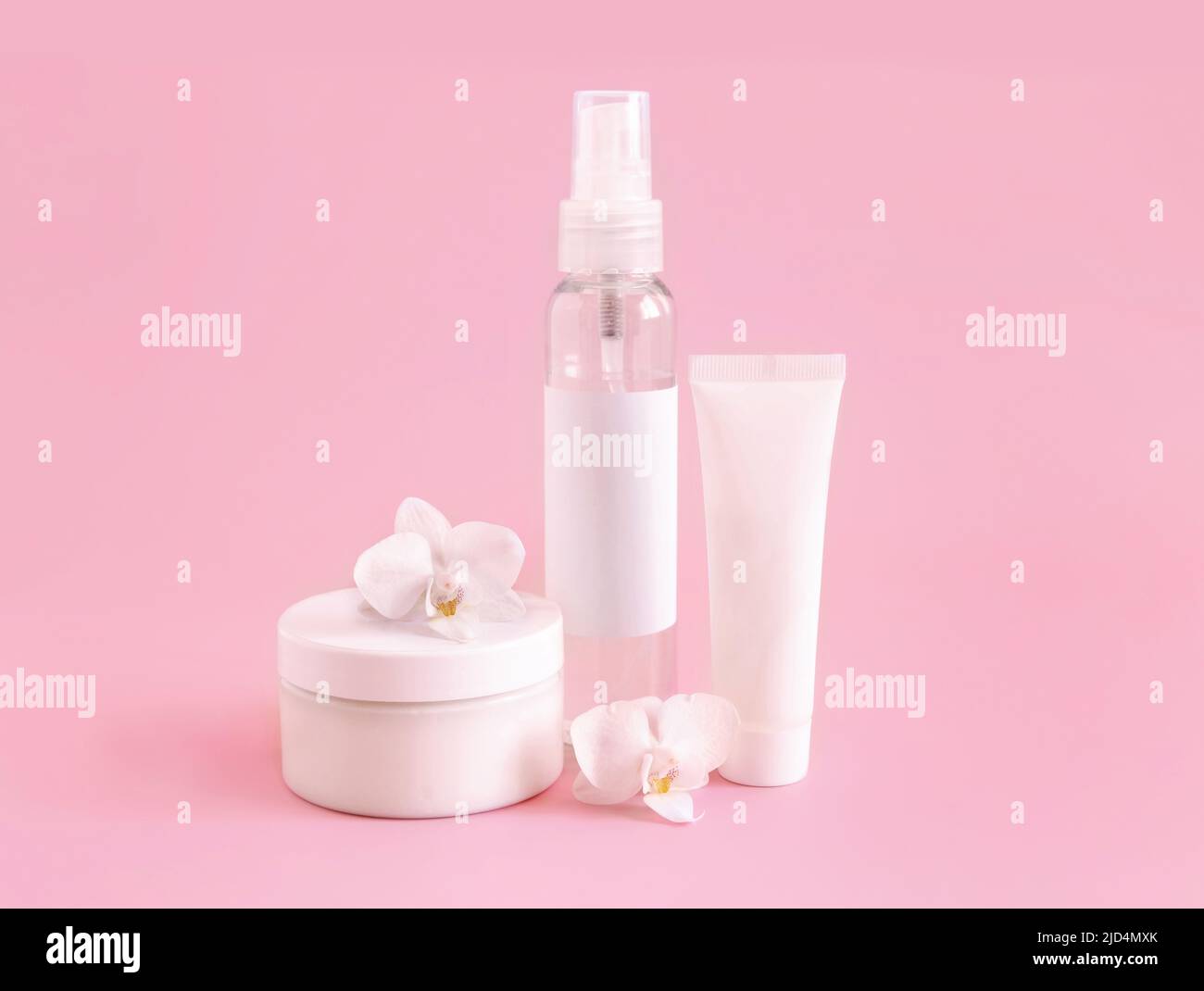 Weißes Kosmetikglas, Tube und Flasche in der Nähe von weißer Orchideenblume auf hellrosa, Nahaufnahme, Mockup. Hautpflegeprodukt, Creme oder Lotion. Exotisch natürlich Stockfoto