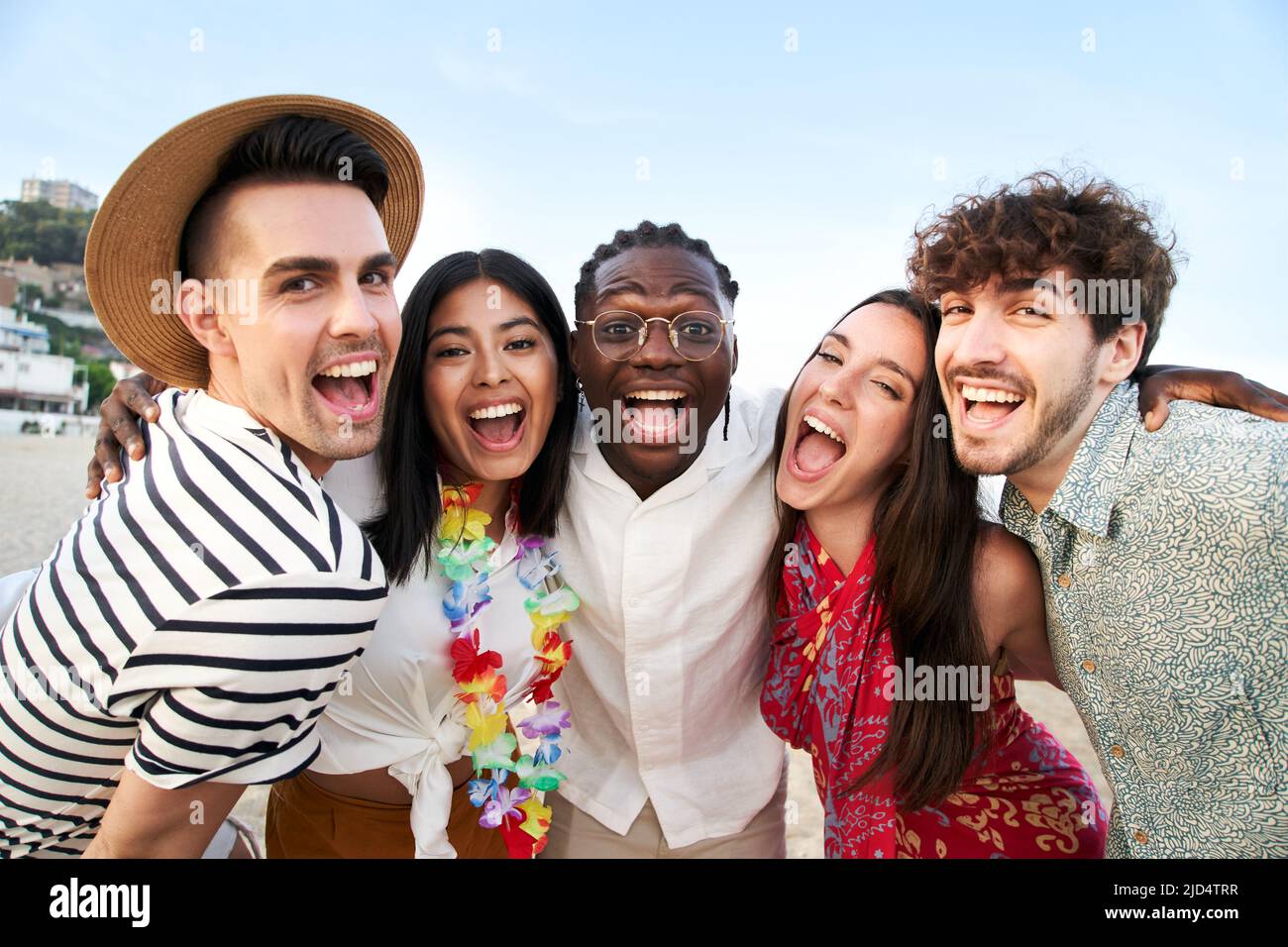 Porträt, das die Kamera von fünf lächelnden Freunden betrachtet, die die Sommerferien genießen. Gruppe von Menschen, die am Strand Freundschaft genießen. Junge Männer und Stockfoto