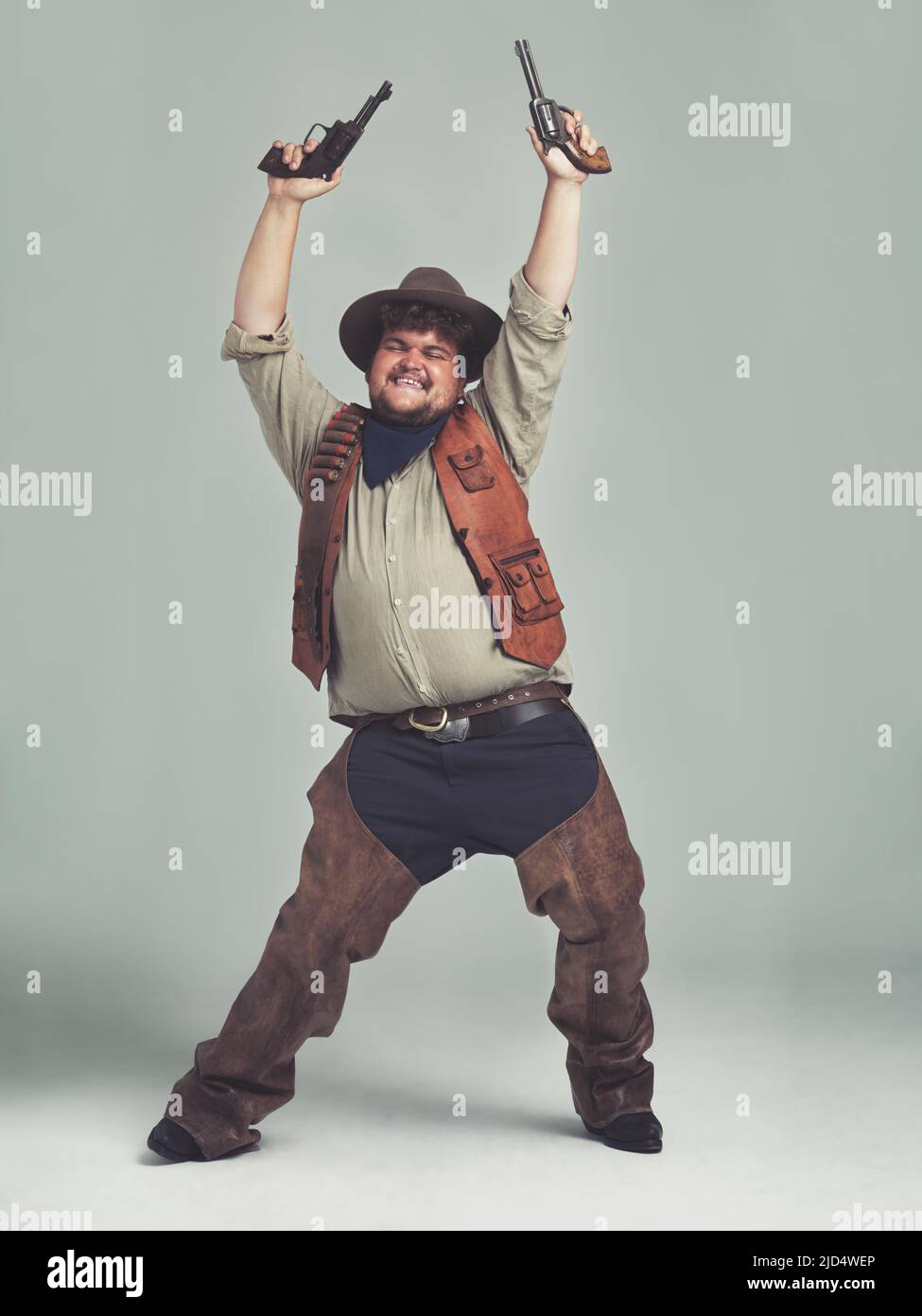 Er hörte, dass die Dorfleute einen neuen Cowboy brauchten Ein übergewichtiger Cowboy, der mit seinen Pistolen in der Luft ekstatisch aussieht. Stockfoto