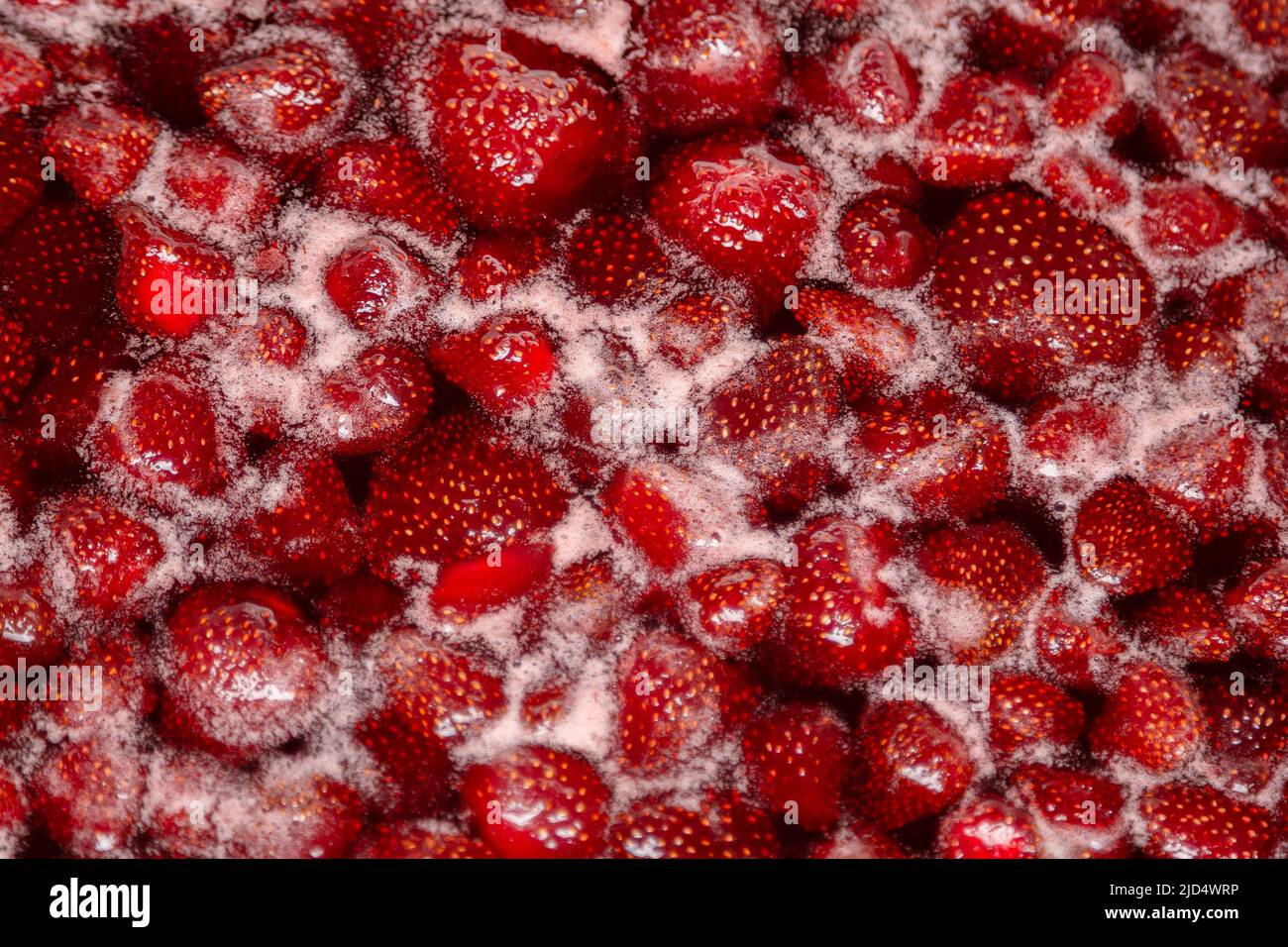 Leicht köchelende Erdbeermarmelade, detaillierte Nahaufnahme, Draufsicht. Schöne Erdbeermarmelade im Kochprozess. Kochende hausgemachte Erdbeermarmelade. Zubereitung einer hausgemachten Erdbeermarmelade. Kochendes Obst in einer Pfanne Stockfoto