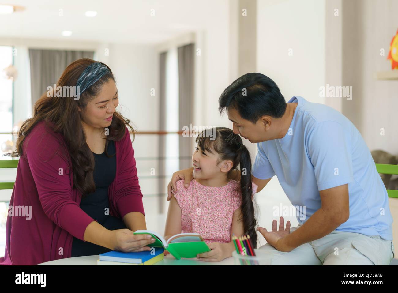 Asiatische Familie mit Vater, Mutter und ihre Tochter lesen Märchen Schwanz Geschichte Buch auf Sofa zu Hause zusammen und zeigt auf das Buch suchen es mit happ Stockfoto