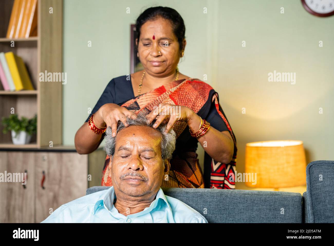 Frau massiert den Kopf eines entspannten Mannes zu Hause, während sie auf dem Sofa sitzt - Konzept der Familie, des älteren Paares und des Bonding. Stockfoto