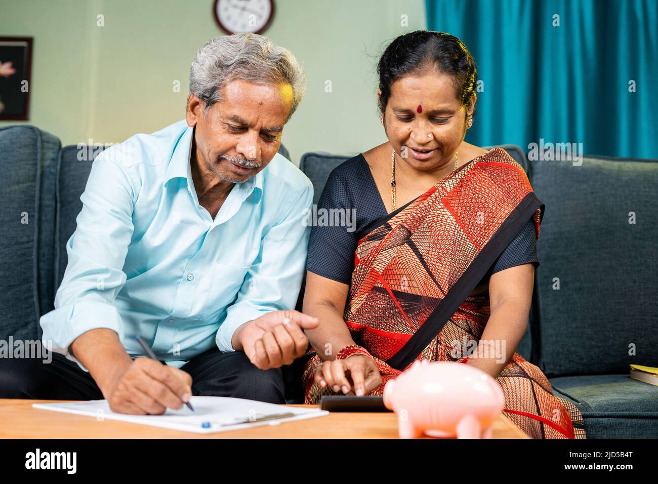 Seniorenpaar beschäftigt Berechnung der Ausgaben oder monatlichen Rechnungen zu Hause, während auf dem Sofa sitzen - Konzept der Planung, Einsparungen, Finanzen und Banken. Stockfoto