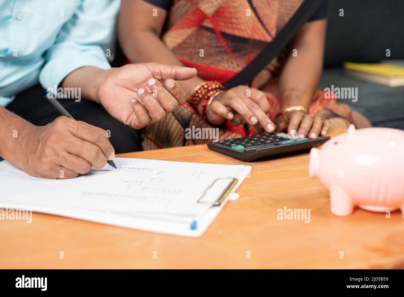 Nahaufnahme der Hände eines älteren Paares, die Ausgaben oder monatliche Rechnungen zu Hause mit Sparschwein berechnen – Konzept der Schulden, Ersparnisse, Finanzen und Banken. Stockfoto