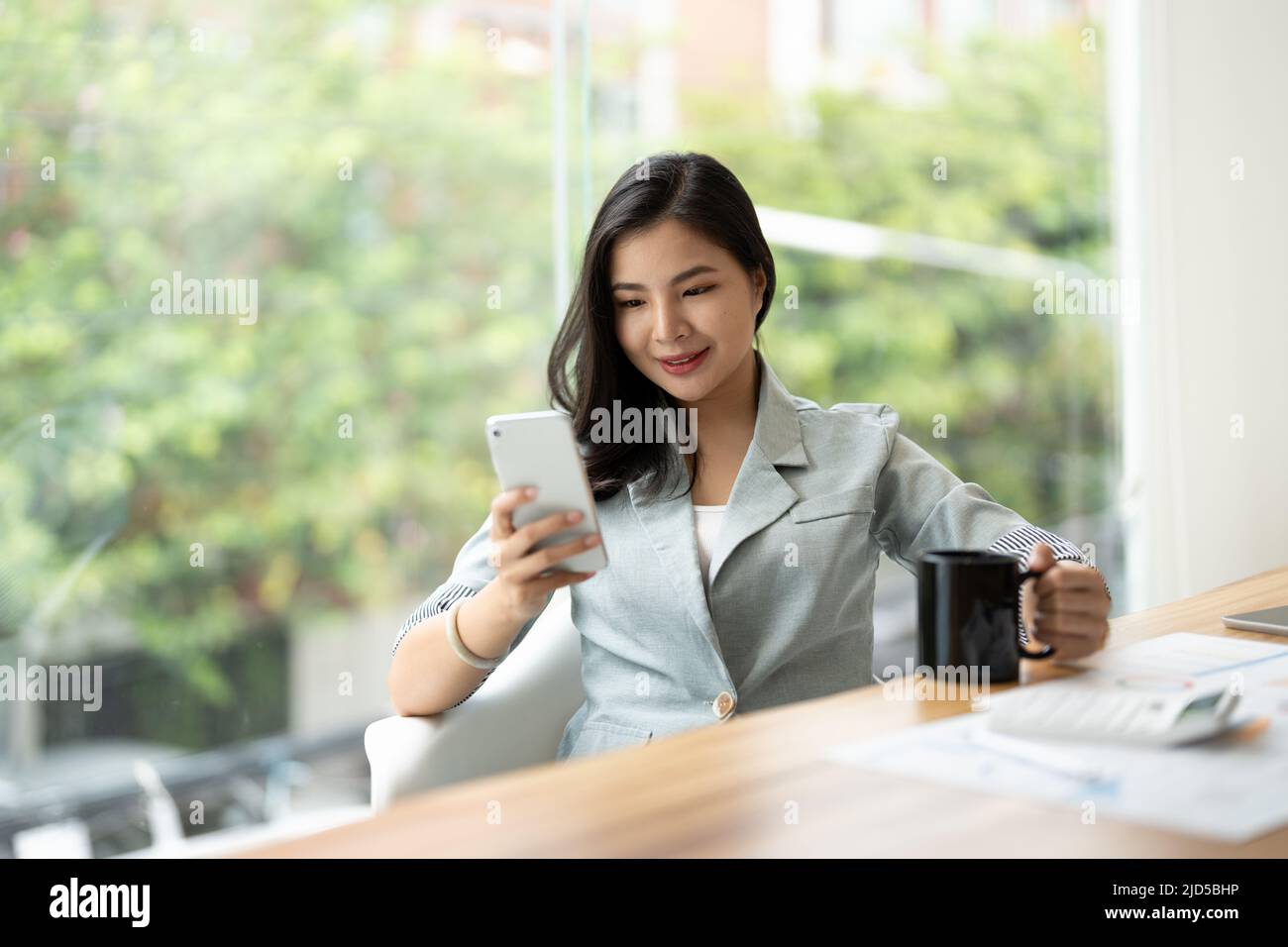 Schöne junge asiatische Geschäftsfrau mit Telefon während der Arbeit mit Rechner und finanzielle Papiere im Büro Stockfoto