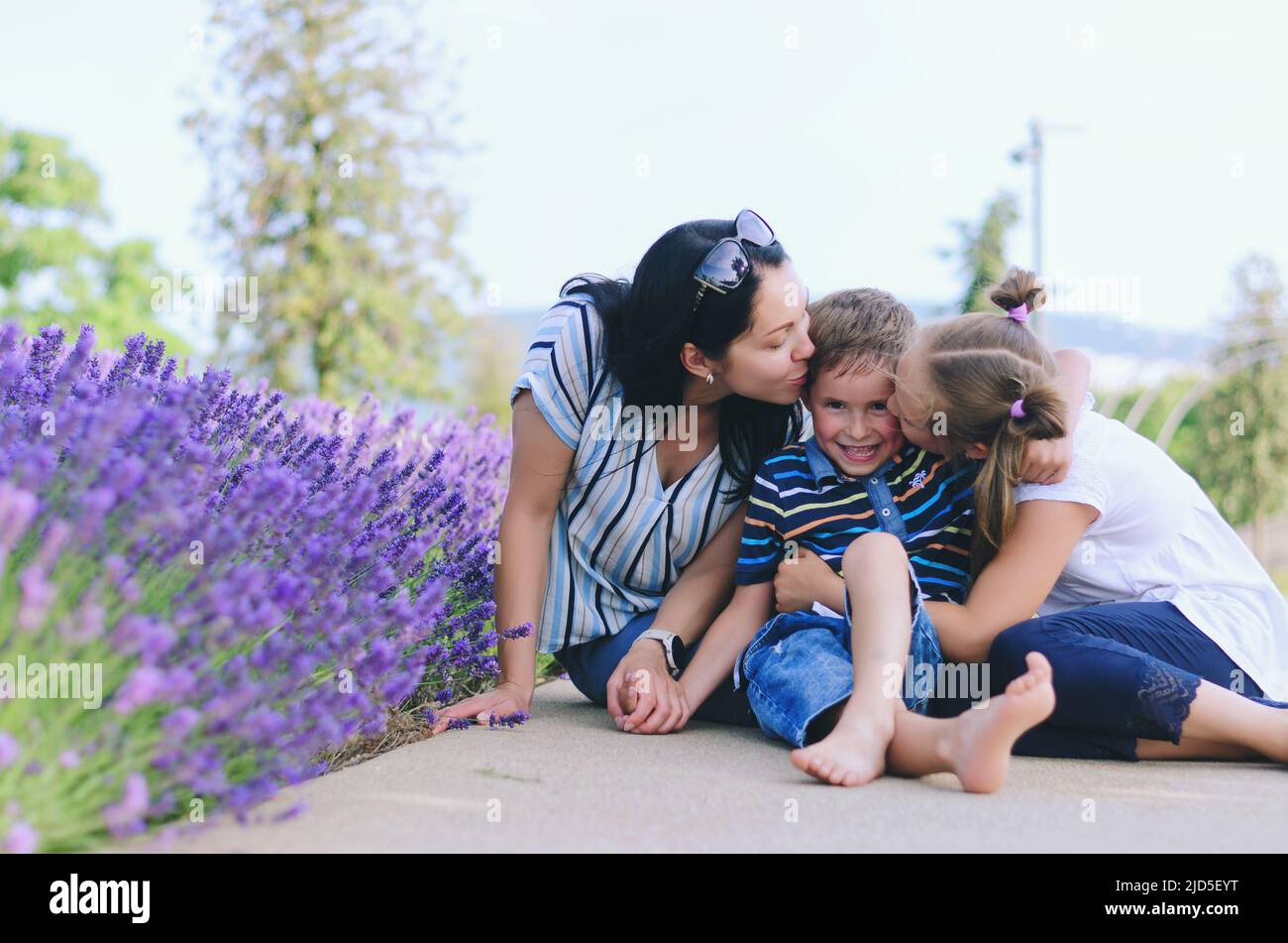 Fröhlicher Familienleben und Urlaubskonzept. Mutter, kleiner Junge, sitzendes Mädchen, Spaziergang in der Altstadt, Straße. Lachend an einem sonnigen Sommertag. Spaß haben Stockfoto