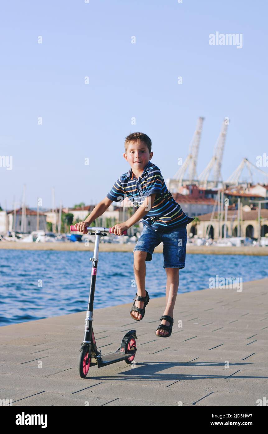 Urlaubskonzept. Kleiner Junge, der Roller reitet, in der Altstadt, Straße zu Fuß. Lachen an einem sonnigen Sommertag. Spaß haben Stockfoto