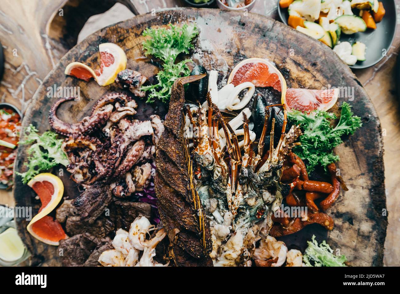 Gourmet-Mittagessen auf einem Holztablett mit Hummer aus Stein, Meeresfrüchten und Obstgarnitur im Beach Club Stockfoto