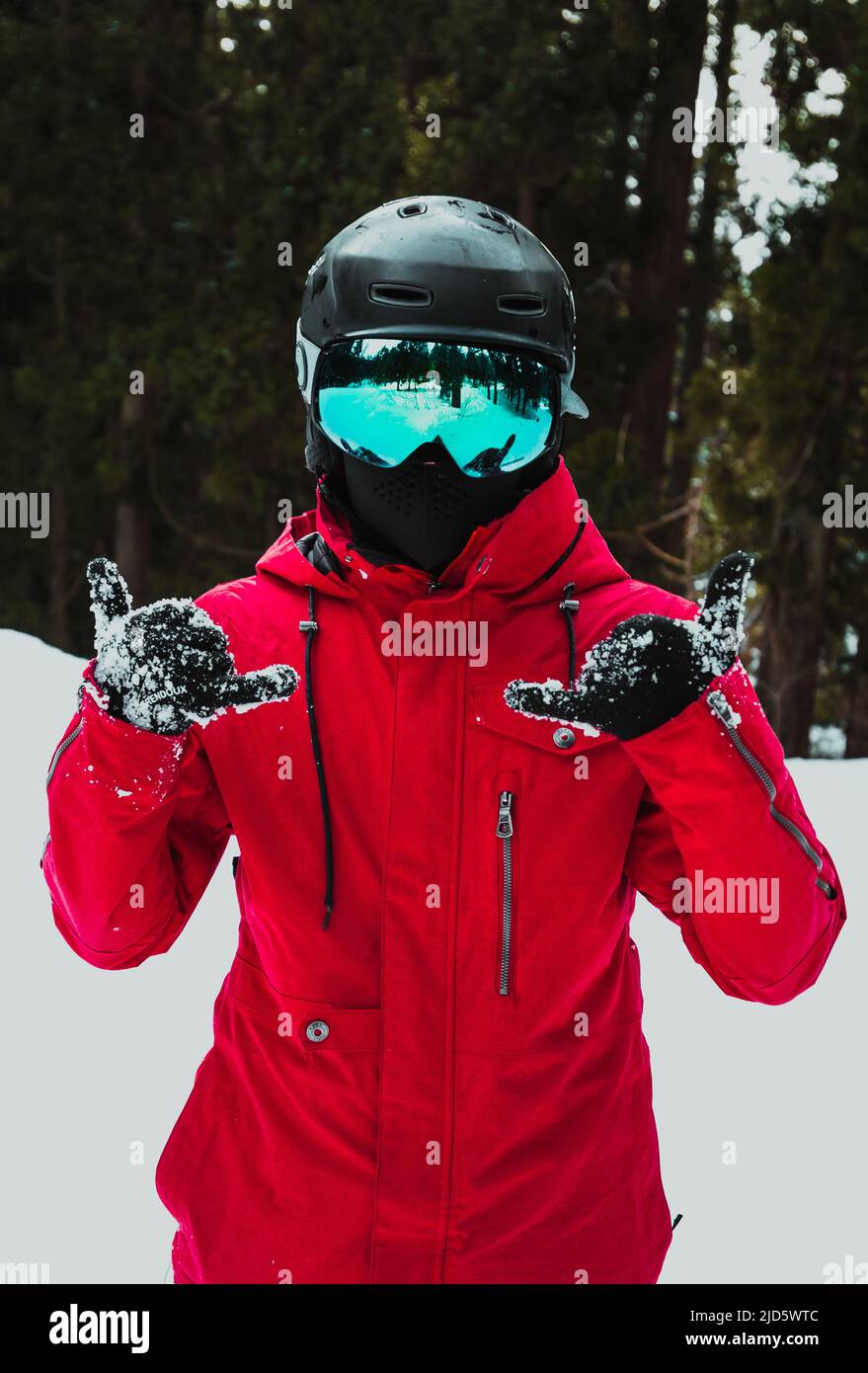Mann auf schneebedecktem Winterberg in roter Jacke, schwarzem Helm und blauer Skibrille Stockfoto