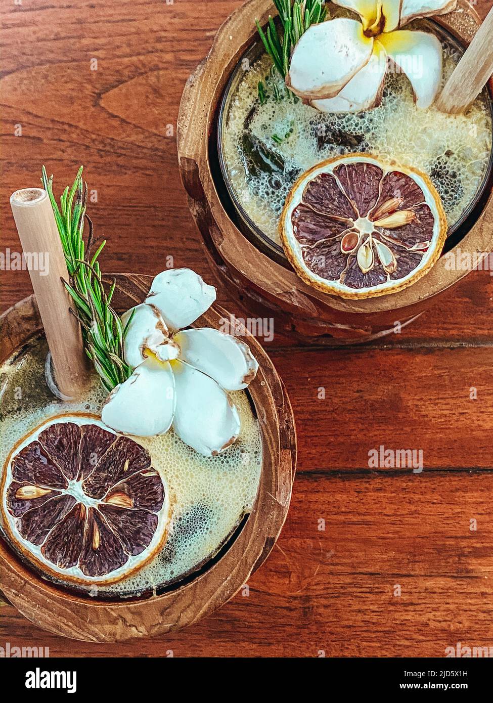 Zwei tropische Cocktailgetränke in Holzbecher mit Orangenschale und Blumenarranierung Stockfoto