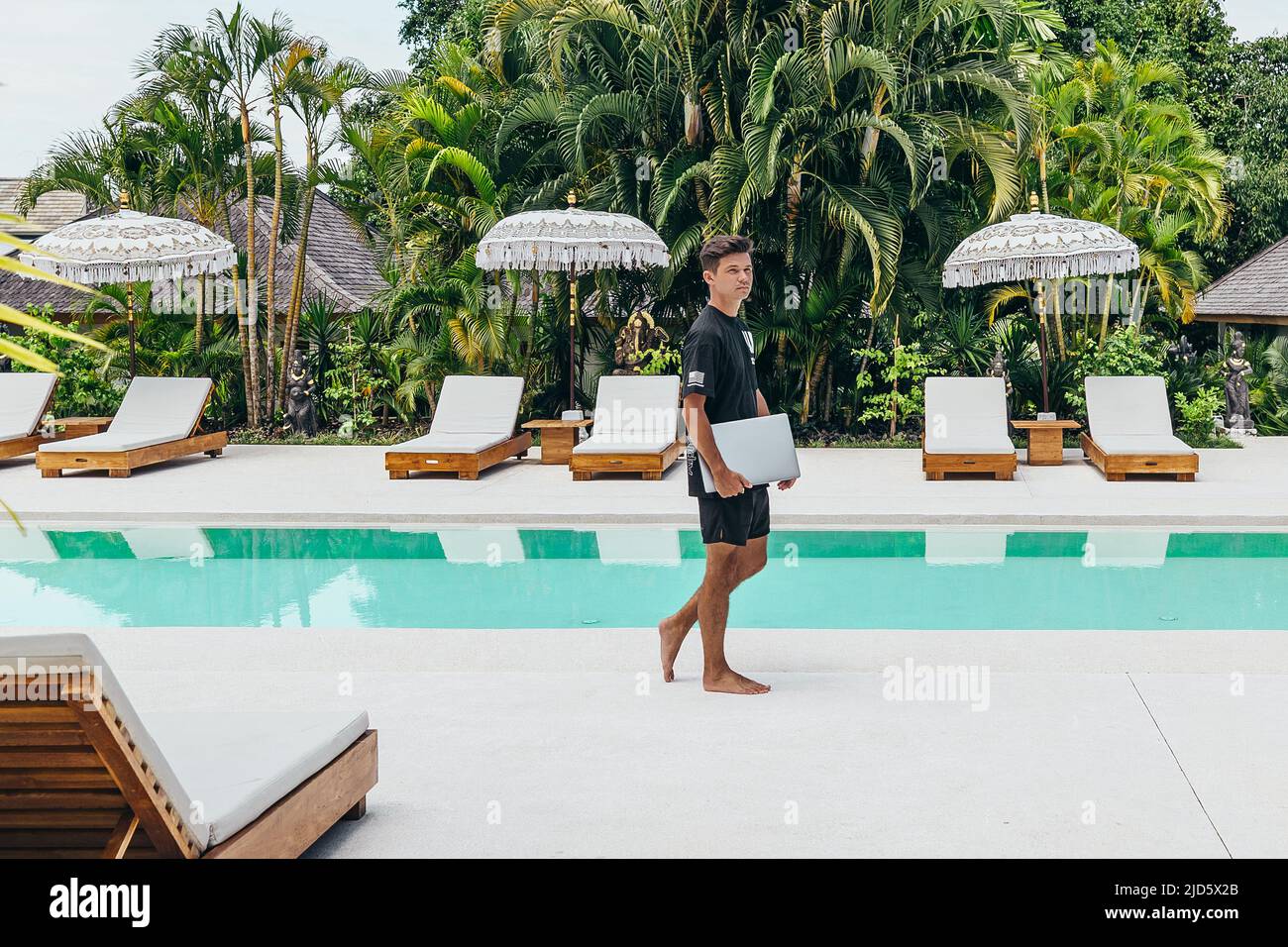 Junger digitaler Nomade, der auf Bali mit einem silbernen Laptop in der Hand arbeitet Stockfoto