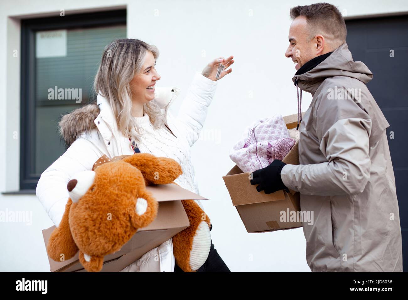 Porträt einer jungen lächelnden Familienfrau und eines Mannes, der die Schlüssel vor der Kamera hält und sich in der Nähe zum neuen Haus vor der Tür bewegt Stockfoto