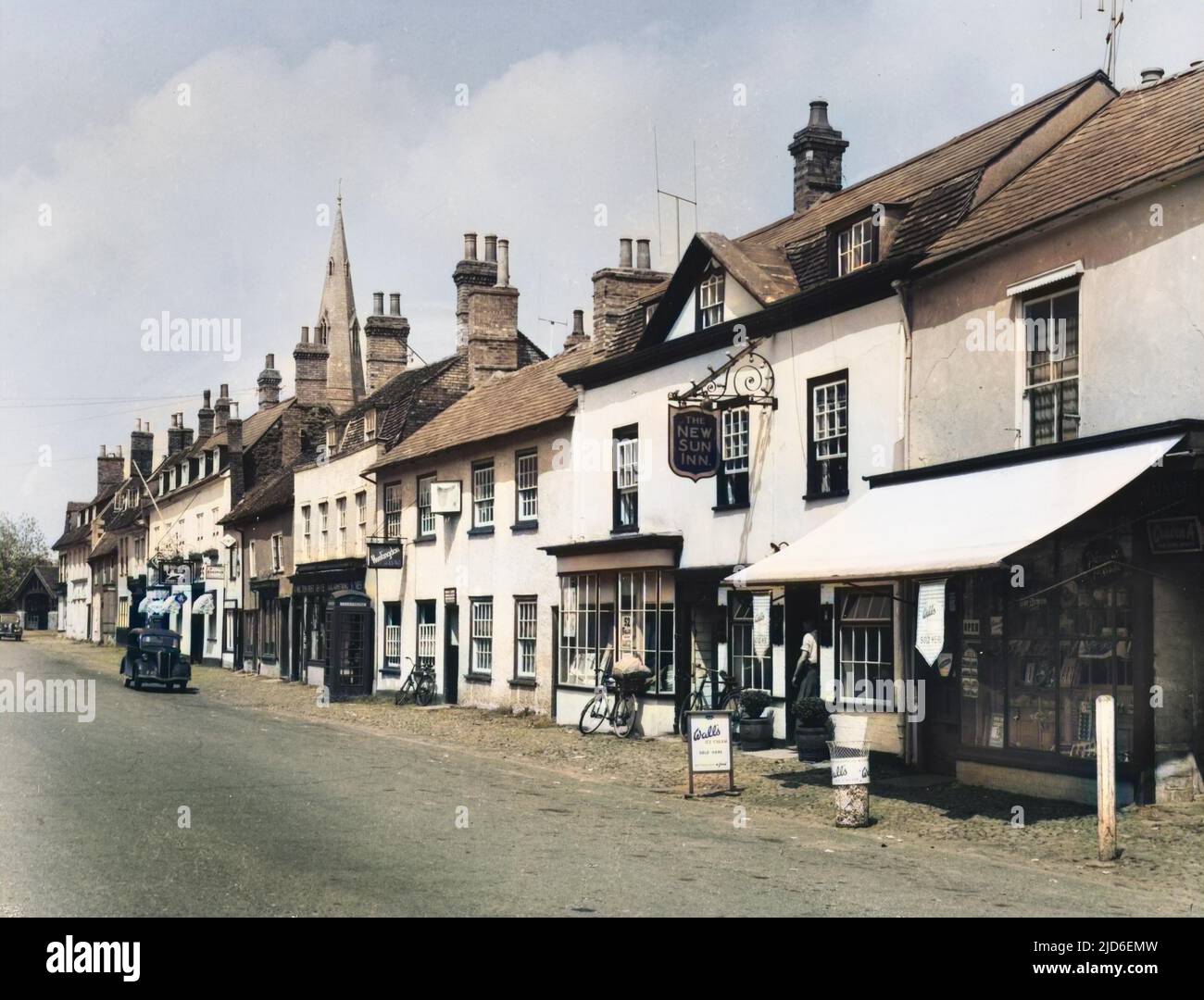 Das angenehme Dorf Kimbolton, Cambridgeshire, England, mit seiner breiten Hauptstraße und charmanten alten weißen Geschäften. Kolorierte Version von : 10153968 Datum: 1940s Stockfoto