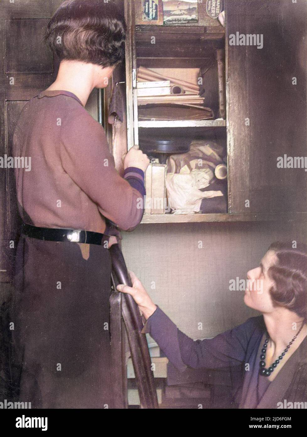 Zwei junge Frauen schauen in einer Widrigkeiten und enden Schrank in einer Ecke unter der Treppe. Kolorierte Version von : 10165129 Datum: Anfang 1930s Stockfoto
