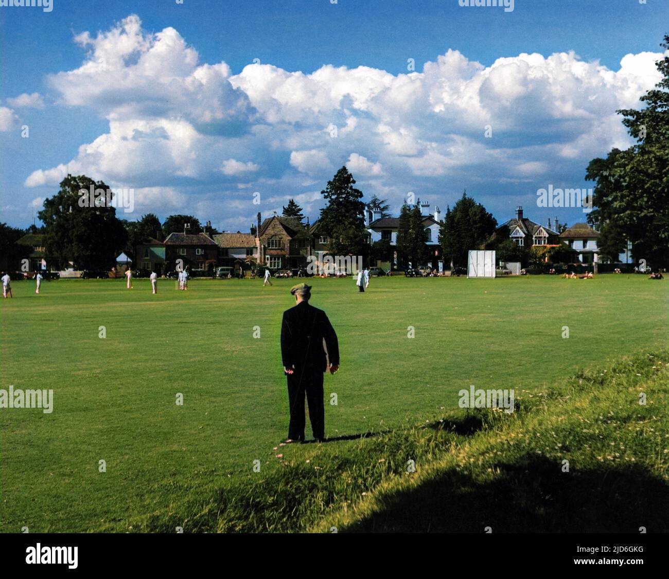Ein alter Mann mit flacher Kappe steht und sieht sich ein Cricket-Spiel an, das auf Giggs Hill Green, Thames Ditton, Surrey, England, gespielt wird. Kolorierte Version von : 10182728 Datum: 1950s Stockfoto