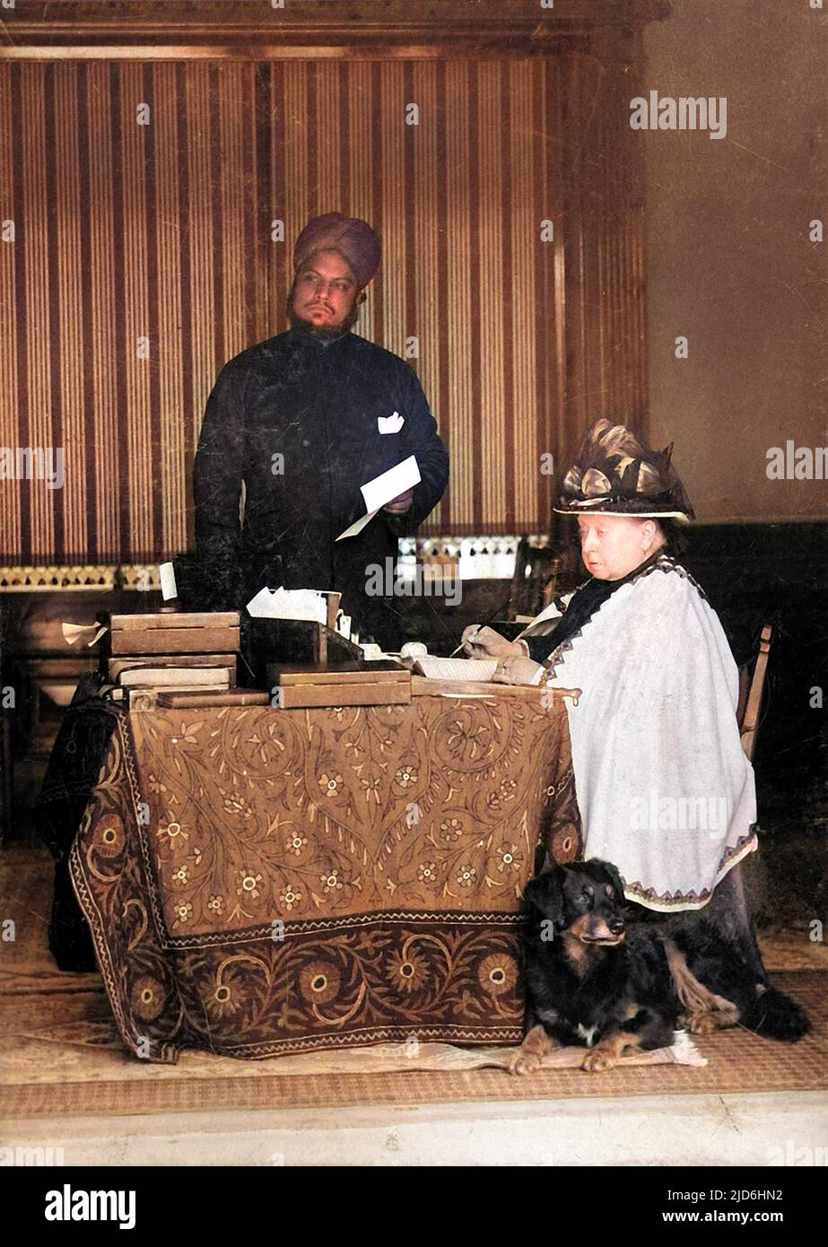 Königin Victoria (1819 - 1901), von Großbritannien und Irland und Kaiserin von Indien, abgebildet am Schreibtisch. Ihr indischer Diener Abdul Karim, auch bekannt als die 'Munshi', steht im Hintergrund. Kolorierte Version von: 10220925 Datum: 1897 Stockfoto