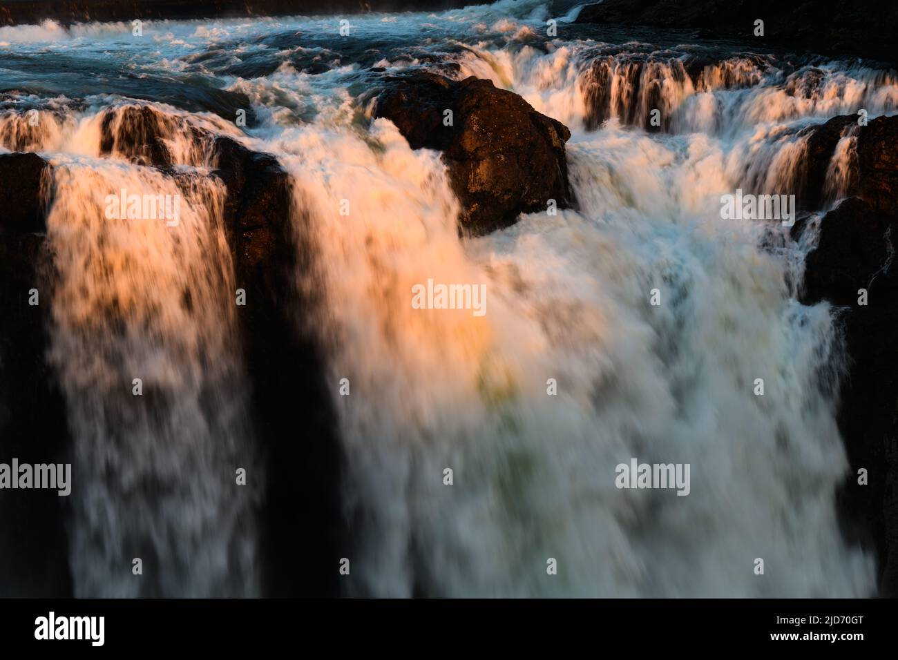 Der letzte orange Schein der untergehenden Sonne erleuchtet den Kamm der Snoqualmie Falls, wenn das Wasser kräftig fällt Stockfoto
