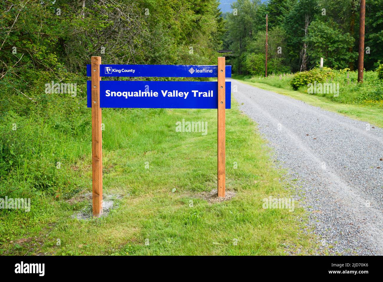 North Bend, WA, USA - 16. Juni 2022; Blaues Schild auf Holzpfosten für den Snoqualmie Valley Trail mit ehemaligem Schotterschienenbett Stockfoto