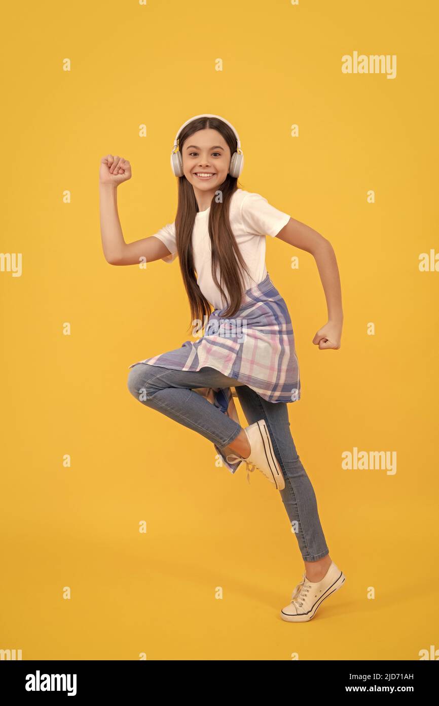 Energisches Teenager-Mädchen läuft, während Musik in Kopfhörern gelben Hintergrund hören, Spaß Stockfoto