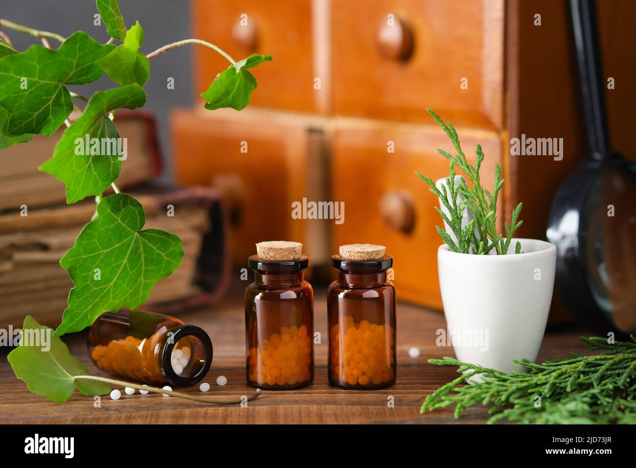 Flaschen mit Homöopathie-Granulat, Schrank mit homöopathischen Mitteln und alte Bücher auf dem Hintergrund. Konzept der Homöopathie. Stockfoto