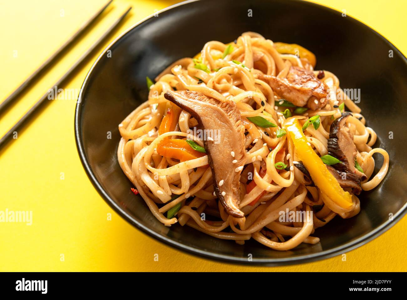 Ein traditionelles asiatisches Gericht. Chinesische udon-Nudeln auf einem schwarzen Teller auf gelbem Hintergrund Stockfoto