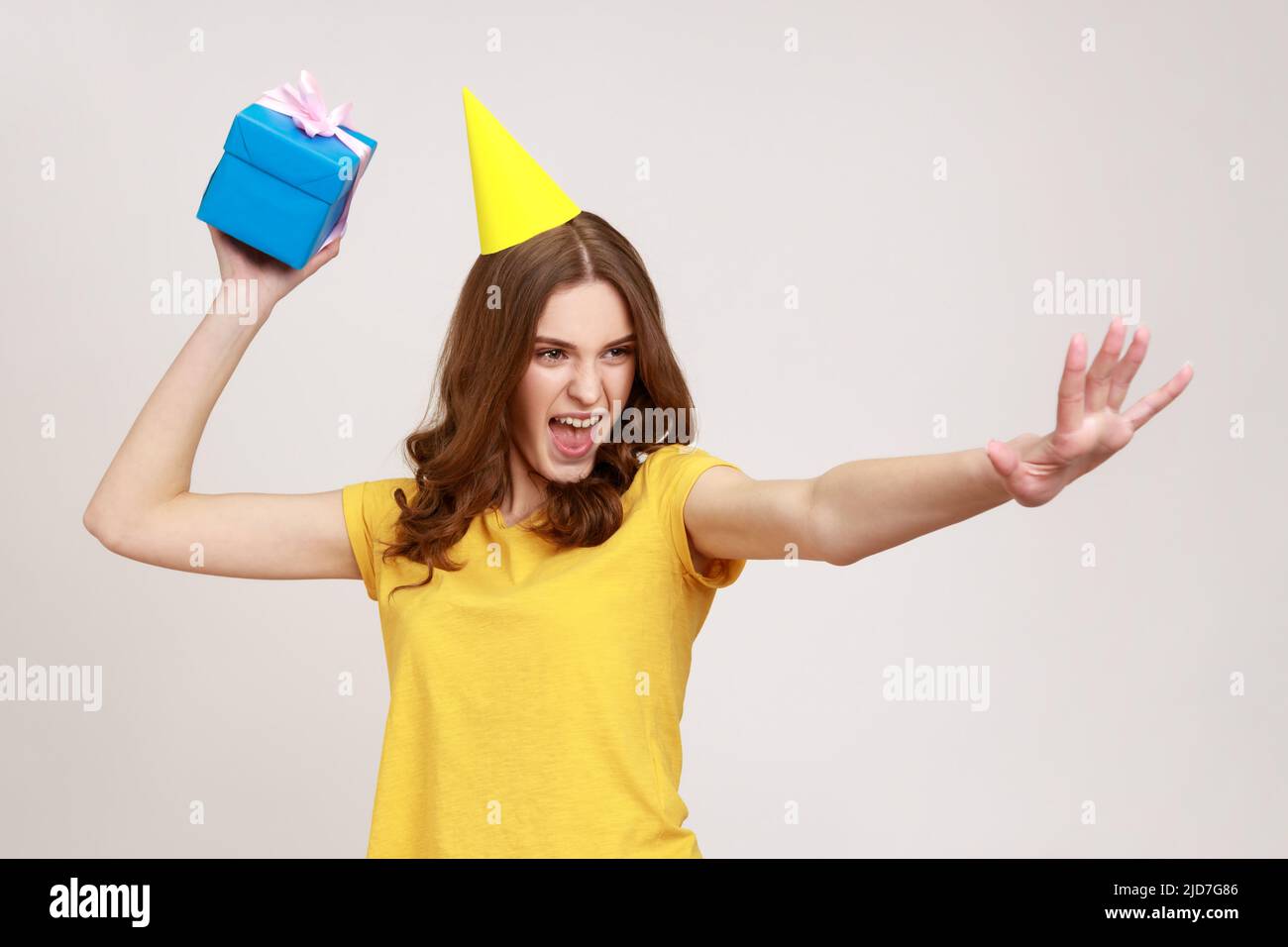 Fangen Sie Ihr Geschenk ein. Nehmt es. Glücklich sorglos junge Frau in gelben T-Shirt bereit, Geburtstagsbox zu werfen, Spaß und Sharing-Geschenk. Innenaufnahme des Studios isoliert auf grauem Hintergrund. Stockfoto