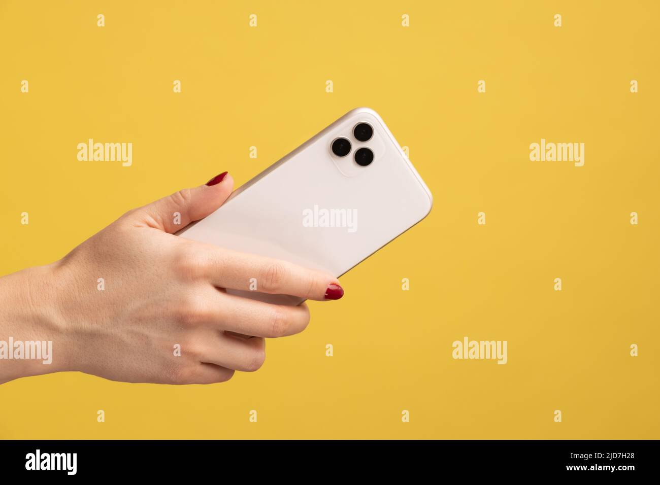 Nahaufnahme Profil Porträt einer Frau Hand halten Handy, zeigt Rückseite des Handys. Innenaufnahme des Studios isoliert auf gelbem Hintergrund. Stockfoto