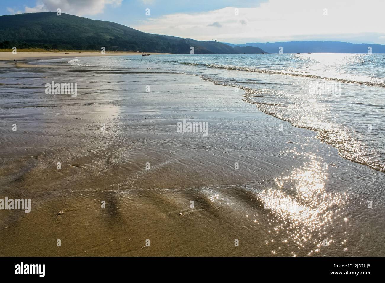 Einsamer Strand mit sanften Wellen auf dem Sand und Reflexion der Sonne im Wasser. Stockfoto