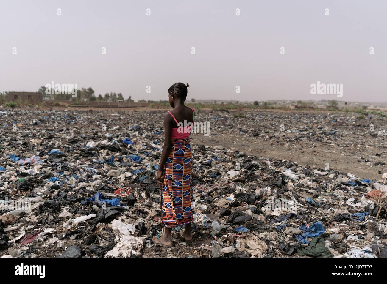 Einsames kleines afrikanisches Mädchen, das auf einer Deponie inmitten aller Arten von Müll steht; Konzept der Umweltverschmutzung Stockfoto