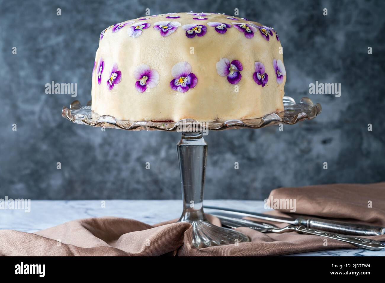 Regenbogenkuchen mit Marzipan bedeckt und mit essbaren Viola-Blüten verziert Stockfoto