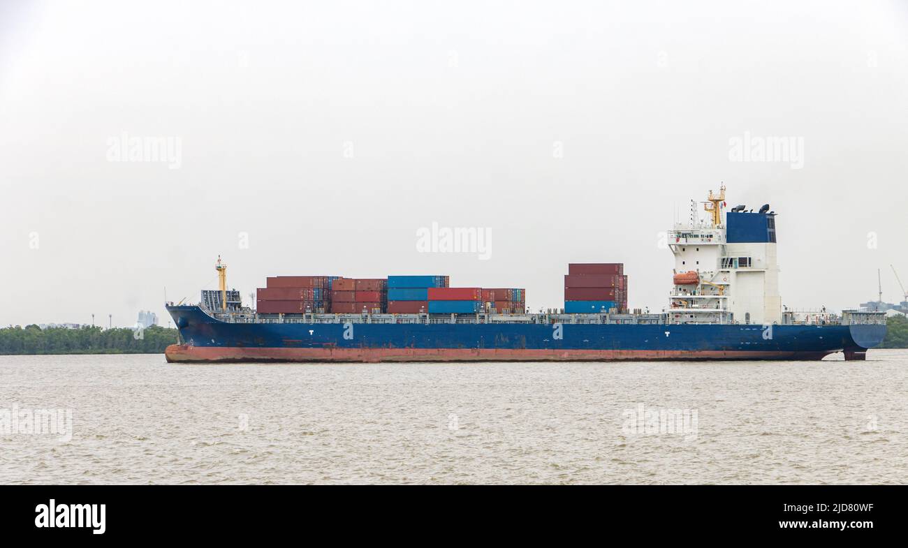 Das Containerschiff, das mit Containern beladen ist, segelt an einer Küste entlang Stockfoto